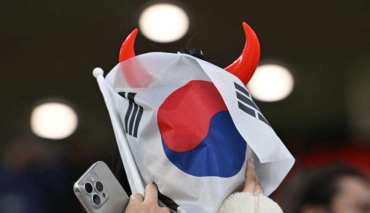 Seorang suporter Korea Selatan menutup muka menggunakan bendera negaranya setelah timnya kalah dari Yordania pada laga semifinal Piala Asia 2023 di Ahmad Bin Ali Stadium, Doha, Qatar, Selasa (06/02/2024). Korea Selatan kalah dengan skor 0-2. (AFP/Hector Retamal)