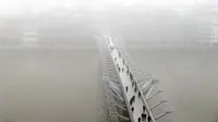 Pejalan kaki berjalan di atas jembatan Millennium Katedral di London, Senin, (23/1). Ribuan penumpang pesawat di Bandara Heathrow terpaksa ditunda keberangkatannya karena cuaca buruk ini. (AP Photo / Kirsty Wigglesworth)