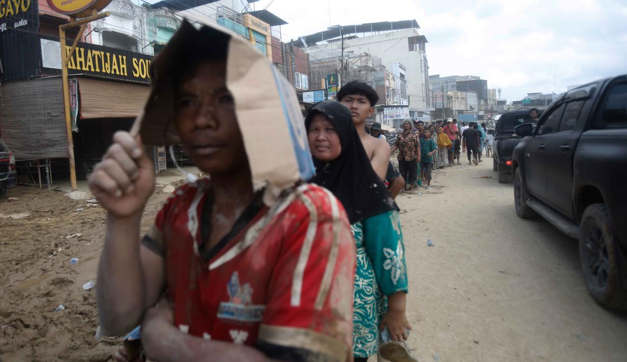 Banyak warga memilih untuk tidur di beberapa titik di pinggir jalan karena faktor rumah hancur sembari menunggu bantuan tiba. Tampak dalam foto, para penyintas mengantre untuk menerima bantuan di daerah yang terdampak banjir bandang di Aceh Tamiang, Sumatra, Jumat 5 Desember 2025. (AP Photo/Binsar Bakkara)