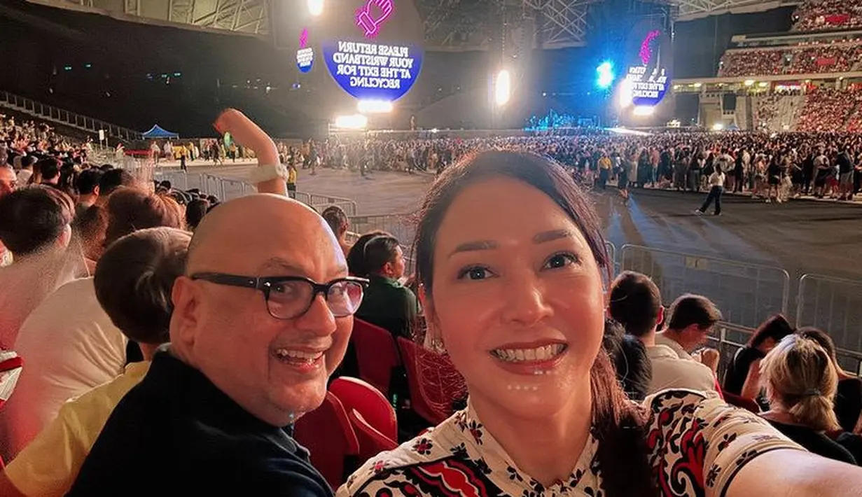 Maia Estianty merayakan ulang tahun dengan menyaksikan Coldplay di Singapura bersama suami. Maia tampil dengan atasan putih bermotif. [@maiaestiantyreal]
