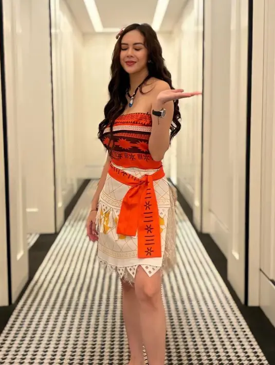 Aura Kasih memilih tampil menjadi Moana. Terlihat dari busana yang dikenakan serba orange lengkap dengan aksesorinya. [@aurakasih]
