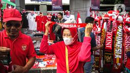 Seorang wanita mengenakan atribut Timnas Indonesia jelang pertandingan AFF 2022 antara Indonesia melawan Thailand di Stadion Gelora Bung Karno, Jakarta, Kamis (29/12/2022). Atribut timnas Indonesia seperti kaos, syal, dan topi dijual dengan kisaran harga Rp35.000 hingga Rp75.000. (Liputan6.com/Faizal Fanani)