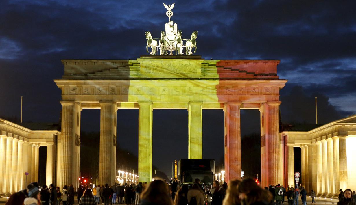 Sejumlah orang berdiri di depan gerbang Brandenburg di Berlin, Jerman, yang berubah warna menjadi bendera Belgia, Selasa (22/3). Hal itu sebagai bentuk penghormatan terhadap korban serangan bom Brussels. (REUTERS/Fabrizio Bensch)