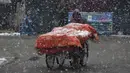 Seorang pria Kashmir mendorong gerobaknya saat salju turun di Srinagar, Kashmir yang dikuasai India (15/1/2020). Menurut pejabat sipil Baseer Khan, Jalur listrik rusak dan banyak jalan terkubur di bawah salju yang mempengaruhi aktivitas warga sehari-hari. (AP Photo/Dar Yasin)