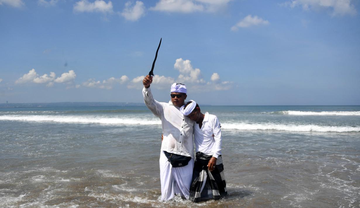 Seorang pria memegang keris saat sembahyang upacara Melasti di pantai Petitenget dekat Denpasar, di pulau resor Bali, Indonesia pada 19 Maret 2023. (AFP/SONNY TUMBELAKA)