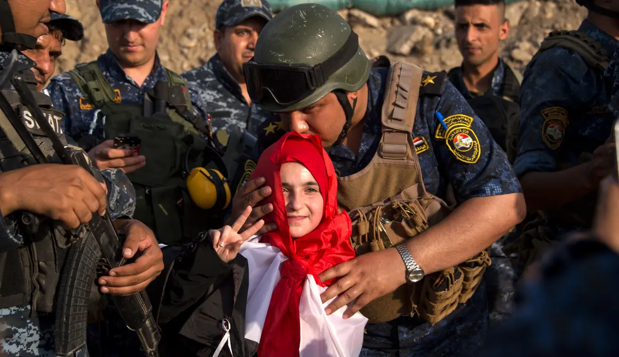 Seorang anggota polisi Federal Irak  mencium seorang anak perempuan saat merayakan keberhasilan mereka menyingkirkan militan ISIS dari Kota Tua Mosul, Minggu (9/7). ISIS merebut Mosul pada musim panas 2014. (FADEL SENNA/AFP)