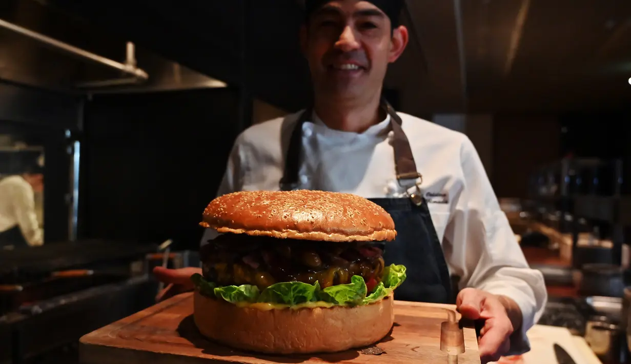 Chef dari restoran The Oak Door, Patrick Shimada berpose dengan burger raksasa di hotel Grand Hyatt Tokyo, Senin (1/4). Golden Giant Burger dibuat untuk memperingati penobatan Putra Mahkota Naruhito pada 1 Mei 2019 dan menandai awal era 'Reiwa' bagi Jepang. (CHARLY TRIBALLEAU/AFP)
