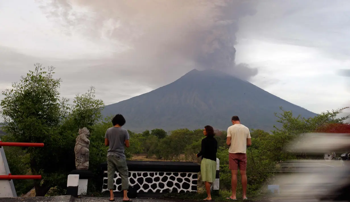 Wisatawan melihat asap Gunung Agung di sebuah kuil di Kabupaten Karangasem, Bali, (27/11). Pihak berwenang telah mengantisipasi dampak yang ditimbulkan oleh aktivitas Gunung Agung dengan menutup Bandara Ngurah Rai. (AP Photo / Firdia Lisnawati)