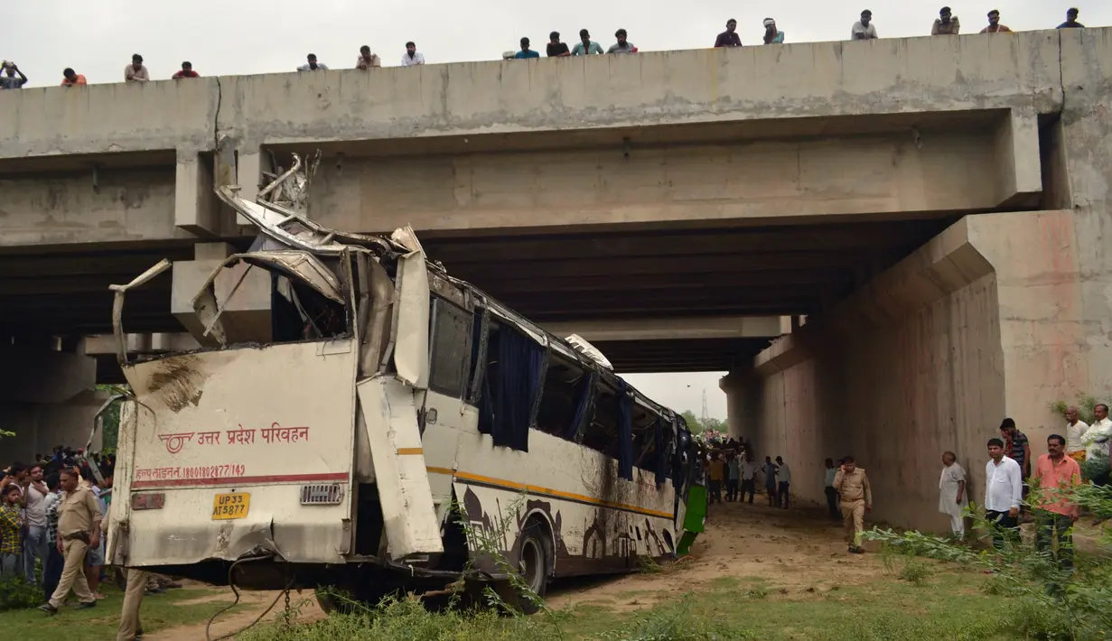 Warga dan polisi menyaksikan bus tingkat yang rusak usai mengalami kecelakaan di jalan bebas hambatan di Agra, India, Senin (8/7/2019). Jalanan di India sering memakan korban lantaran infrastrukturnya terkenal buruk dan pengemudi yang kerap ngebut. (Pawan Sharma/AFP)