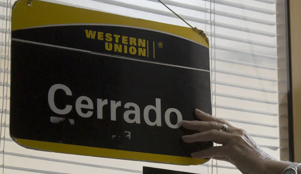 Pekerja kantor Western Union memasang tanda tutup pada hari terakhir bisnisnya di Havana, Kuba, Senin (23/11/2020). Penutupan yang didorong oleh sanksi keras AS itu akan membuat ribuan warga Kuba yang biasa menggunakan jasa perusahaan pengiriman uang tersebut kehilangan akses. (AP/Ismael Francisco)