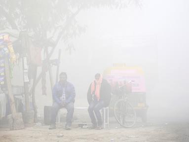 Warga duduk di samping toko saat kabut tebal akibat polusi menyelimuti  Delhi, India (1/12). Kabut ini diklaim sebagai kabut asap terparah yang dialami oleh New Delhi dalam 17 tahun yang telah mengurangi jarak pandang. (REUTERS/Cathal McNaughton)