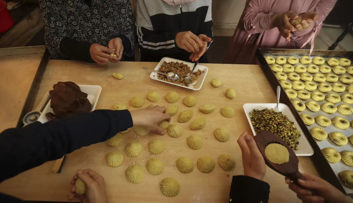 <p>Perempuan Palestina membuat kue tradisional berisi kurma dan kacang-kacangan dalam persiapan untuk liburan Idul Fitri, di kota Hebron, Tepi Barat, pada 28 April 2022. Orang-orang di Palestina mempunyai tradisi lebaran yang unik dan khas yaitu dengan membuat kue kering dengan aneka bentuk dan rasa. (HAZEM BADER / AFP)</p>