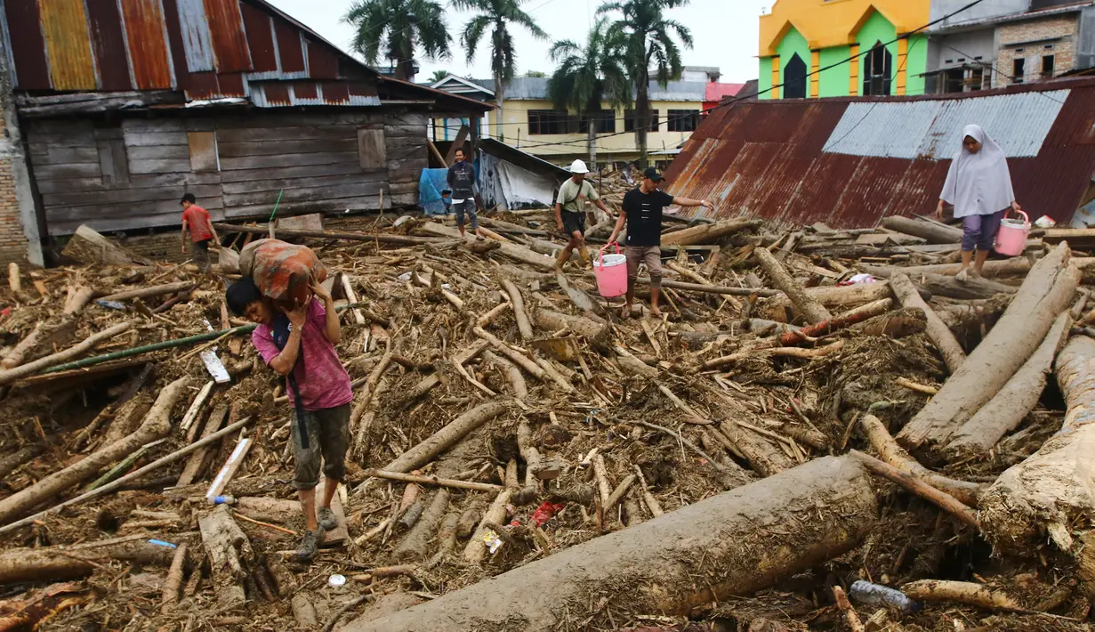 Orang-orang berjalan di atas puing-puing di daerah yang terkena banjir bandang di Masamba, Sulawesi Selatan, Rabu (15/7/2020). Banjir bandang akibat tingginya curah hujan tersebut mengakibatkan 16 orang meninggal dunia dan puluhan warga dilaporkan masih dalam pencarian. (AP/Khaizuran Muchtamir)