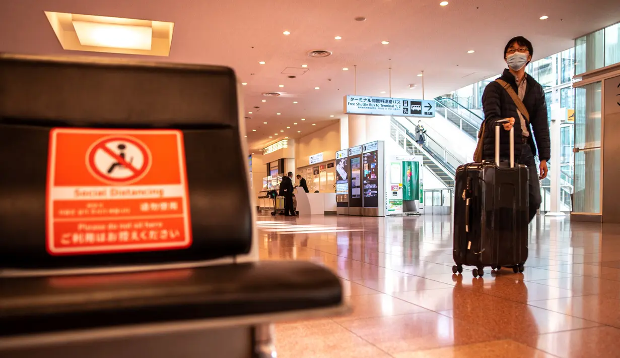 Seorang penumpang berjalan dengan kopernya di aula kedatangan di Bandara Internasional Haneda Tokyo, Jumat (18/2/2022). Pemerintah Jepang mengumumkan rencana untuk melonggarkan aturan perbatasan virus bagi pekerja dan pelajar. (AFP/Philip Fong)