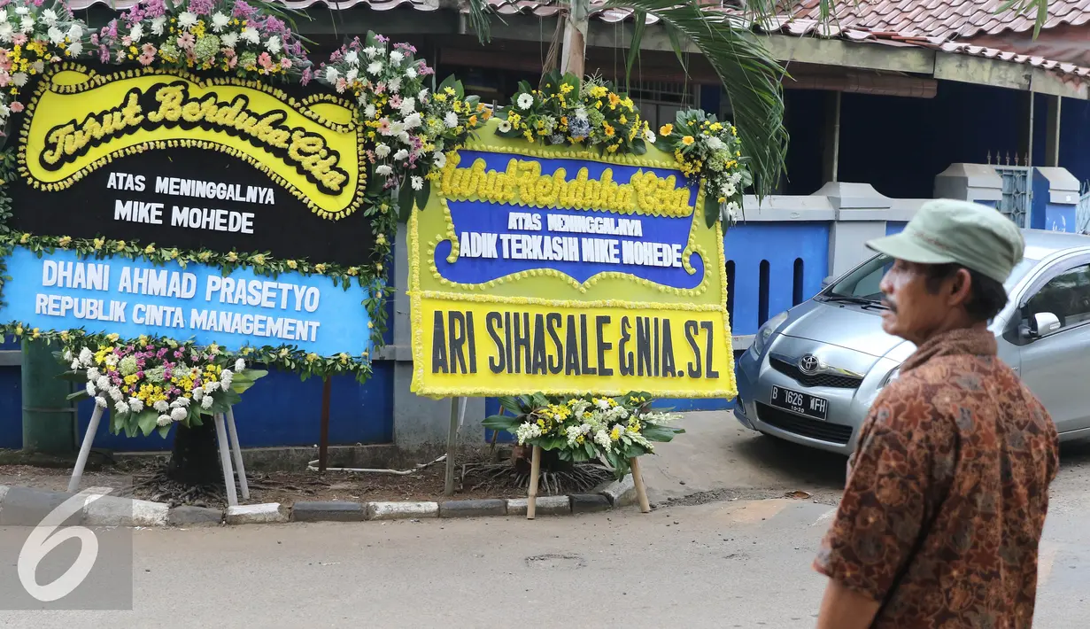 Warga melintasi karangan bunga duka cita wafatnya penyanyi Mike Mohede di kawasan Tangerang Selatan, Banten, Senin (1/8). Mike Mohede mengembuskan napas terakhirnya saat tidur siang di kamar seusai bermain game. (Liputan6.com/Herman Zakharia)