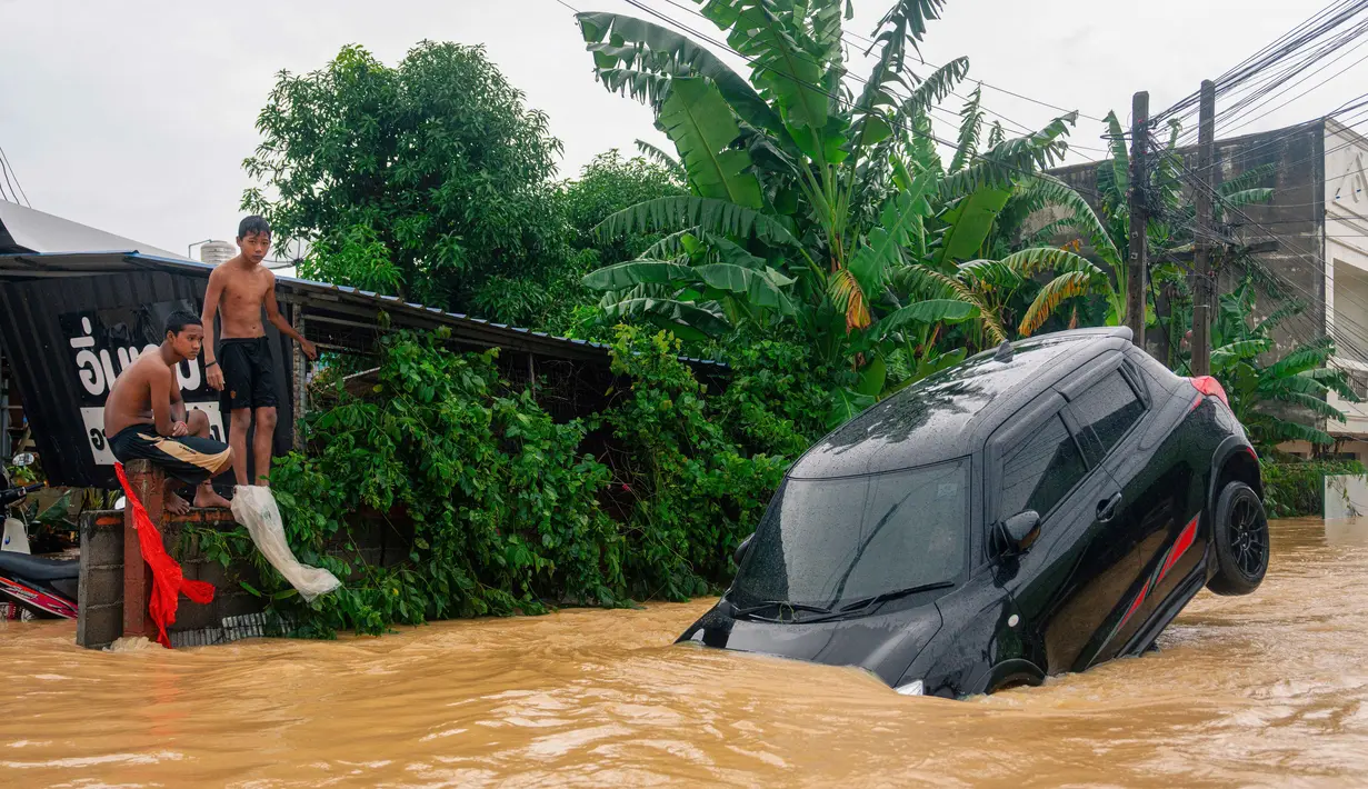 Pihak berwenang telah mengerahkan helikopter dan perahu untuk mengevakuasi warga yang terjebak dan pasien kritis dari lokasi banjir. Tampak dalam foto, dua pemuda melihat sebuah mobil yang terendam banjir tinggi di Hat Yai, Provinsi Songkhla, Thailand selatan, pada Rabu 26 November 2025. (Arnun Chonmahatrakool/THAI NEWS PIX/AFP)
