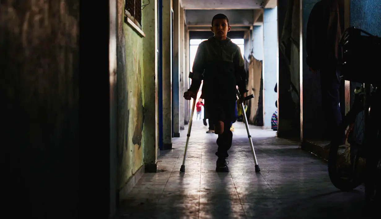 Rateb Mahmoud Qaliq berjalan menggunakan kruk di sepanjang lorong sekolah UNRWA yang telah menjadi tempat penampungan bagi pengungsi Palestina di Deir al-Balah, di Jalur Gaza tengah, pada 3 Desember 2025. Rateb Mahmoud Qaliq merupakan seorang anak laki-laki Palestina berusia sembilan tahun dari Jalur Gaza. (Bashar Taleb/AFP)