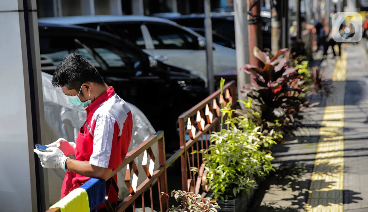 Seorang pegawai bermain ponsel sambil berjemur di bawah sinar matahari di Kawasan Fatmawati, Jakarta, Selasa (31/3/2020). Berjemur diri di bawah sinar matahari saat pagi merupakan salah satu upaya yang paling sederhana untuk menjaga kesehatan selama wabah virus COVID-19. (Liputan6.com/Faizal Fanani)