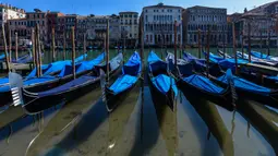 Perairan yang lebih jernih terlihat saat sejumlah gondola terparkir di Grand Canal Venesia pada 18 Maret 2020. Sejak Italia memberlakukan lockdown akibat pandemi virus corona, air di Kanal Venesia yang biasanya keruh dan gelap berubah menjadi jernih. (ANDREA PATTARO / AFP)