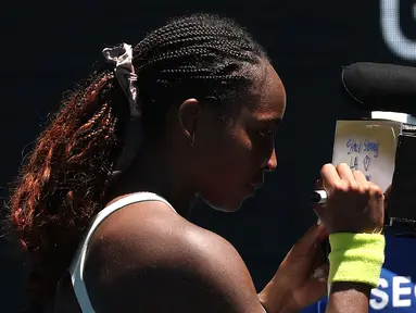 Petenis Amerika Serikat, Coco Gauff menuliskan pesan untuk korban kebakaran dan pemadam kebakaran di Los Angeles, Amerika setelah menang atas kompatriotnya, Sofia Kenin pada hari kedua Australia Open 2025 di Melbourne, Australia, Senin (13/01/2025). (AFP/David Gray)