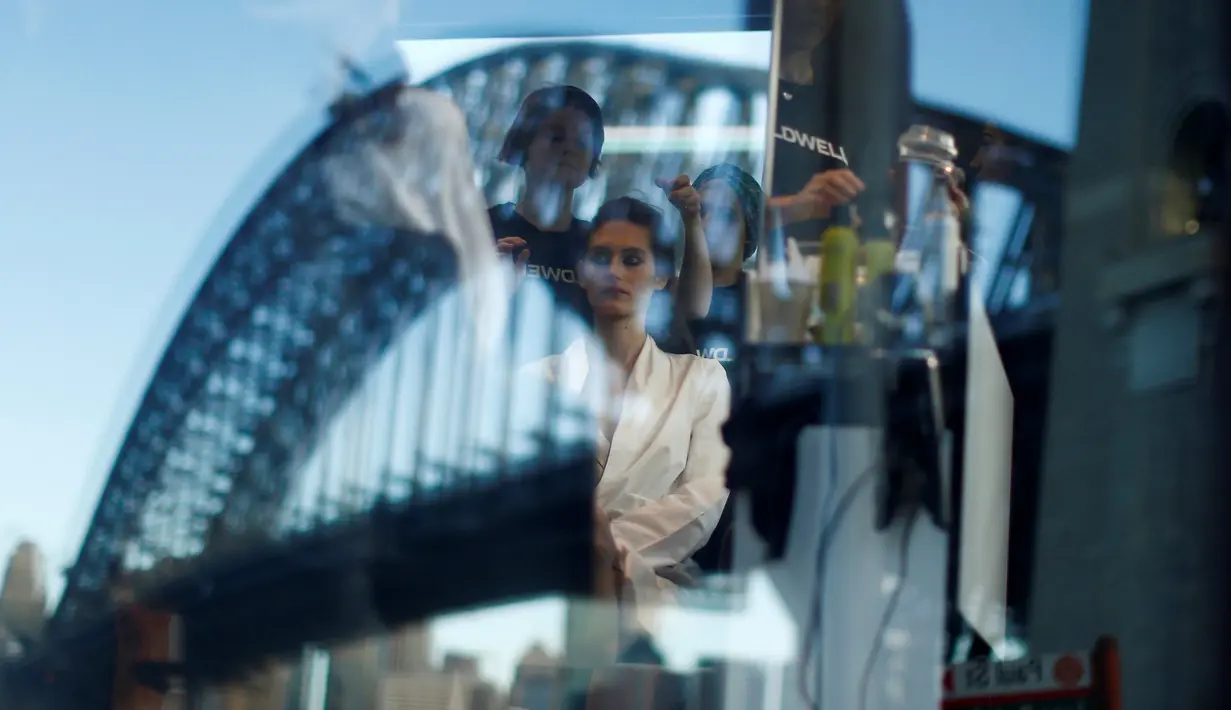 Seorang model terlihat di cermin sedang ditata rambutnya sebelum memperagakan busana Manning Cartell di bawah jembatan Sydney Harbour Bridge dalam acara Australian Fashion week, 17 Mei 2016. (REUTERS/Jason Reed)