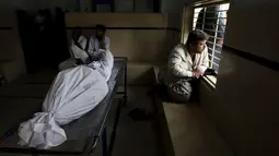 Seorang kerabat duduk dekat jenazah korban gelombang panas sambil menungggu ambulans, di sebuah kamar mayat di Karachi, Pakistan, Senin (22/6). Fenomena gelombang panas yang mendera Pakistan telah menewaskan setidaknya 120 orang. (REUTERS/Akhtar Soomro)