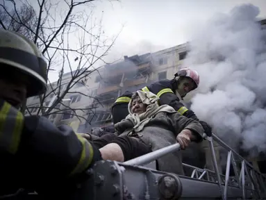 Petugas pemadam kebakaran mengevakuasi seorang wanita tua dari gedung apartemen yang terkena tembakan di Kyiv, Ukraina (14/3/2022). Dua orang tewas pada 14 Maret 2022 akibat serangan penembakan dan rudal Rusia yang menghancurkan gedung apartemen tersebut. (Ukrainian State Emergency Service via AP)