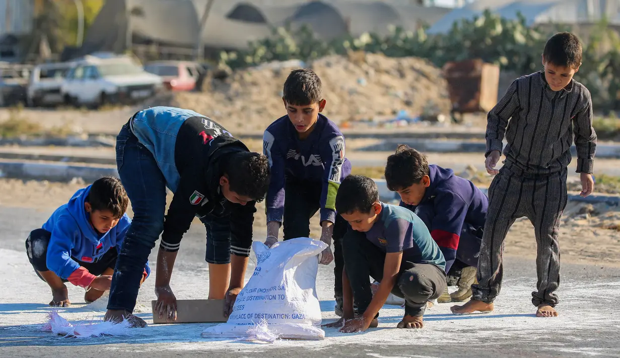 Anak laki-laki Palestina mengais tepung dari jalan setelah sebuah tas jatuh dari truk bantuan yang melaju di jalan Salaheddin di Deir el-Balah di Jalur Gaza tengah pada 5 November 2024. (Eyad BABA/AFP)
