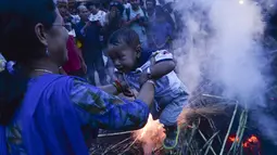 Seorang ibu mengasapi anaknya di sisa pembakaran patung iblis Ghantakarna selama Ghantakarna di kota kuno Bhaktapur, Nepal (30/7/2019). Ritual ini untuk merayakan kekalahan iblis dalam mitos Ghantakarna yang menyimbolkan penghancuran kejahatan. (AFP Photo/Prakash Mathema)
