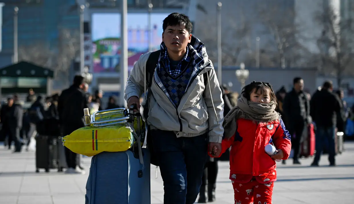 Seorang pria menggandeng bocah sambil membawa koper berjalan ke pintu masuk stasiun kereta api Beijing, Jumat (10/1/2020). Puluhan ribu warga China telah meninggalkan kota-kota besar China menuju kampung halaman, guna merayakan Tahun Baru Imlek pada 25 Januari mendatang. (WANG ZHAO/AFP)