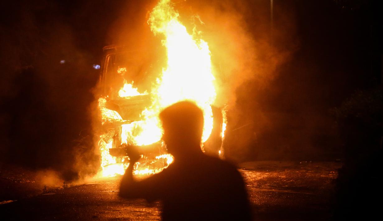 Seseorang melewati kendaraan polisi yang terbakar setelah ribuan pengunjuk rasa marah dengan pemberlakuan kembali jam malam Covid-19 pada akhir pekan di depan gedung Majelis Nasional di Beograd, Selasa (7/7/2020). Mereka mengecam cara pemerintah mengatasi pandemi Covid-19. (OLIVER BUNIC/AFP)