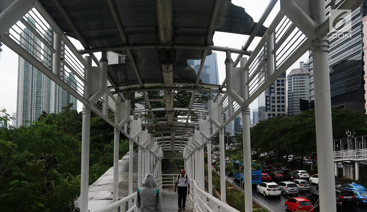 Warga melintasi Jembatan Penyeberangan Orang (JPO) yang rusak di kawasan Dukuh Atas, Jakarta, Rabu (12/12). Hingga saat ini, atap JPO Dukuh Atas yang rusak belum juga diperbaiki. (Liputan6.com/JohanTallo)