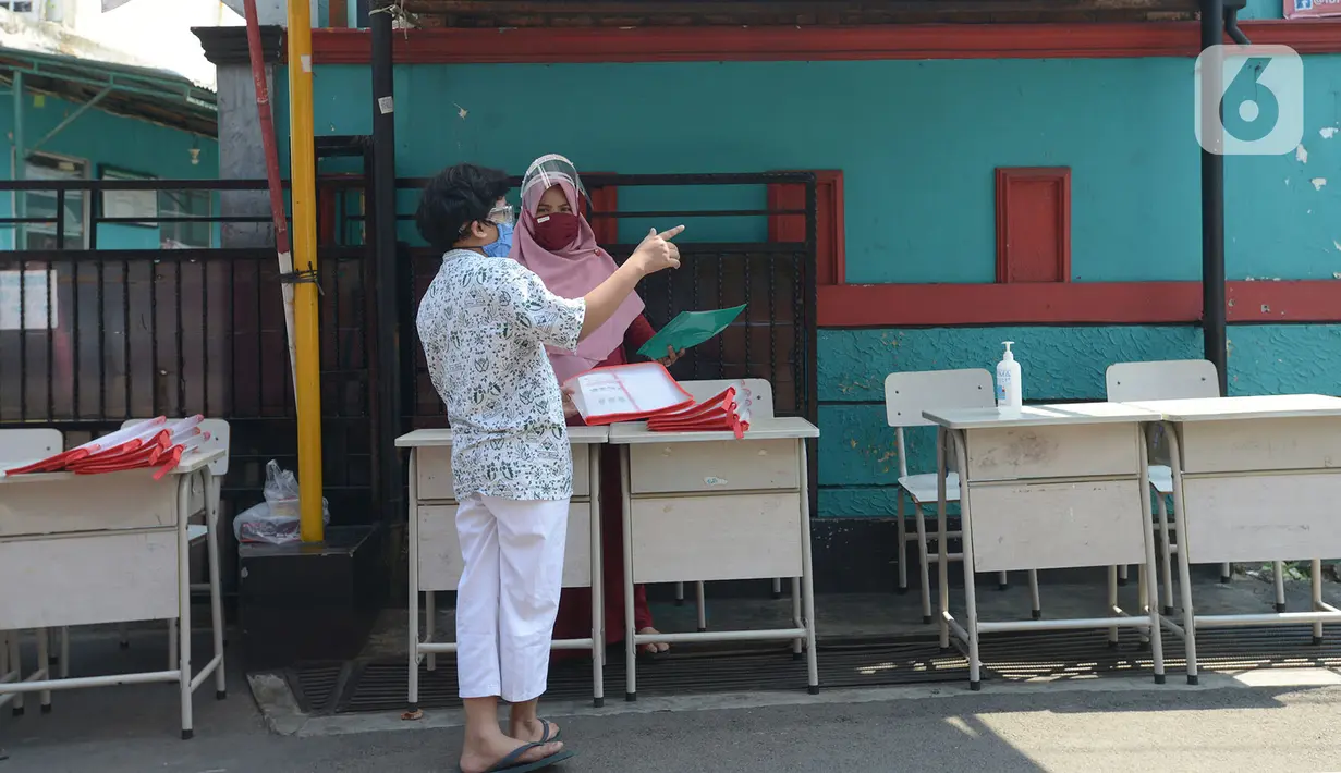 Guru SDIT Ibnu Sina memberikan tugas sekolah secara drive-thru kepada wali murid di Jakarta, Rabu (26/8/2020). Tugas sekolah tersebut dikerjakan oleh siswa dalam satu minggu agar penilaian dan proses belajar mengajar tetap berlangsung. (merdeka.com/Imam Buhori)