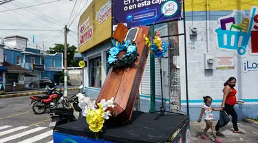 Warga berjalan dekat peti mati dengan tulisan, "Anda memutuskan, di rumah atau di dalam kotak ini", sebagai bagian dari kampanye pemerintah setempat di jalan-jalan kotamadya Escuintla, Guatemala City pada 21 Juli 2020. Kampanye itu sebagai upaya menghentikan penyebaran COVID-19. (Johan ORDONEZ/AFP)