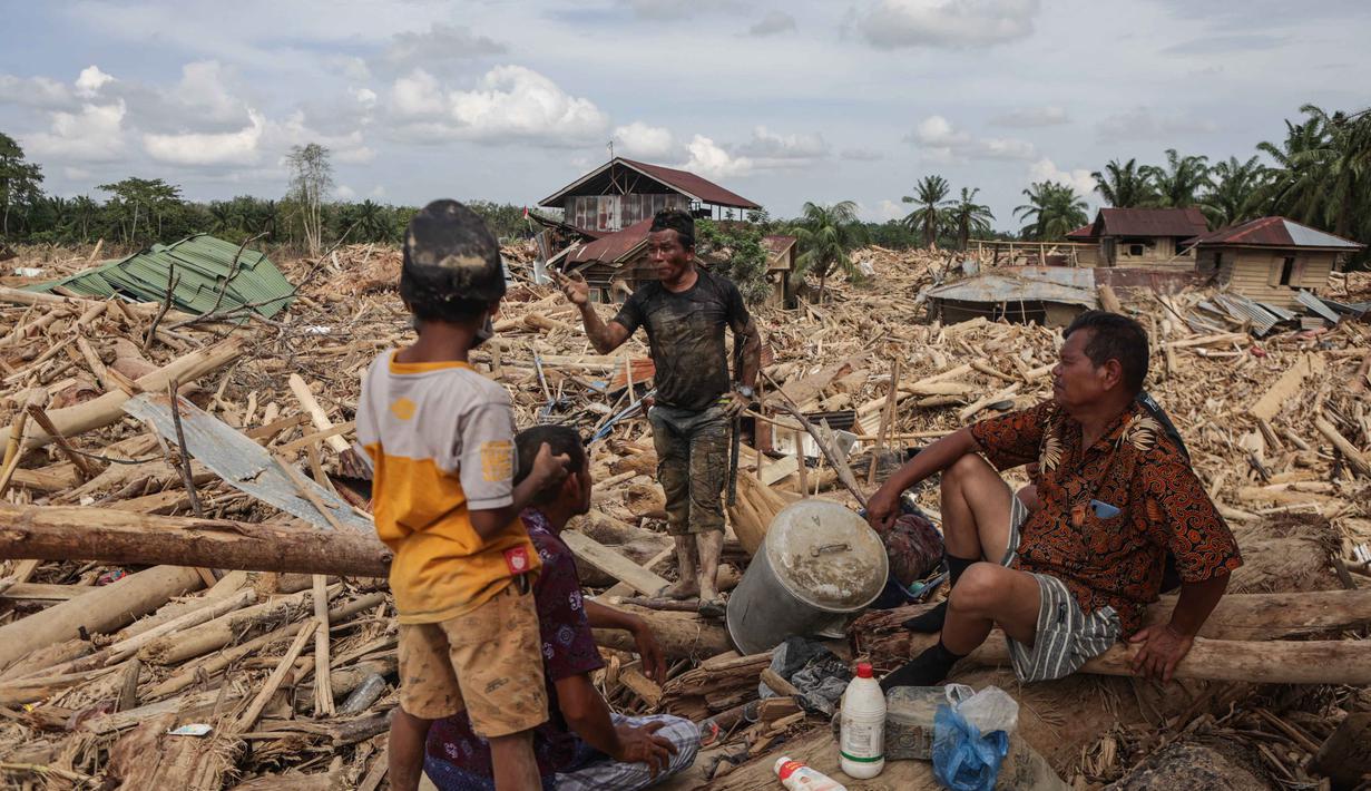 Di desa Lintang Baru, Aceh Tamiang, ada banyak rumah dan bangunan hilang tertimbun kayu gelondongan dan material lumpur yang mulai mengeras. Tampak dalam foto, warga beristirahat sambil mencari sisa-sisa rumah mereka yang terkubur di bawah tumpukan pohon tumbang yang disapu banjir bandang, di desa Lintang Baru di Aceh Tamiang, Sumatera Utara, pada Kamis 11 Desember 2025. (Aditya Aji/AFP)