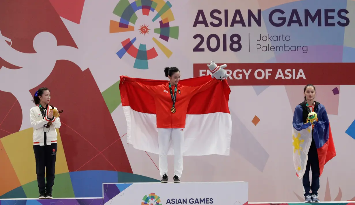 Atlet Wushu Indonesia, Lindswell Kwok (tengah) membentangkan bendera Merah Putih setelah berhasil meraih emas  pada Asian Games, Jakarta, Senin, (20/8). Lindswell berhasil menyumbang emas kedua untuk Indonesia di Asian Games 2018. (AP Photo/Aaron Favila)