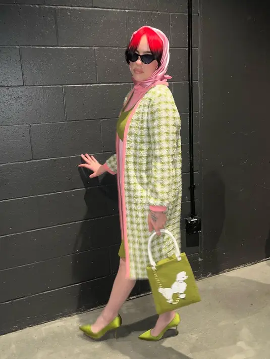 Penampilannya kemudian dilengkapi dengan stocking dan kerudung satin warna merah muda senada, tote bag anjing poodle, dan satin pointed heels warna hijau.  [@billieeilish/@andrewmukamal]