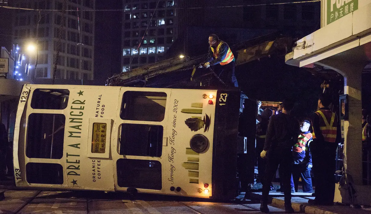 Regu penolong berusaha mengevakuasi trem double-decker yang terbalik di jalan utama di Hong Kong, Kamis (6/4). Belum jelas penyebab kecelakaan, namun kemungkinan akibat pengemudi gagal mengendalikan kendaraan tersebut. (ANTHONY WALLACE/AFP)