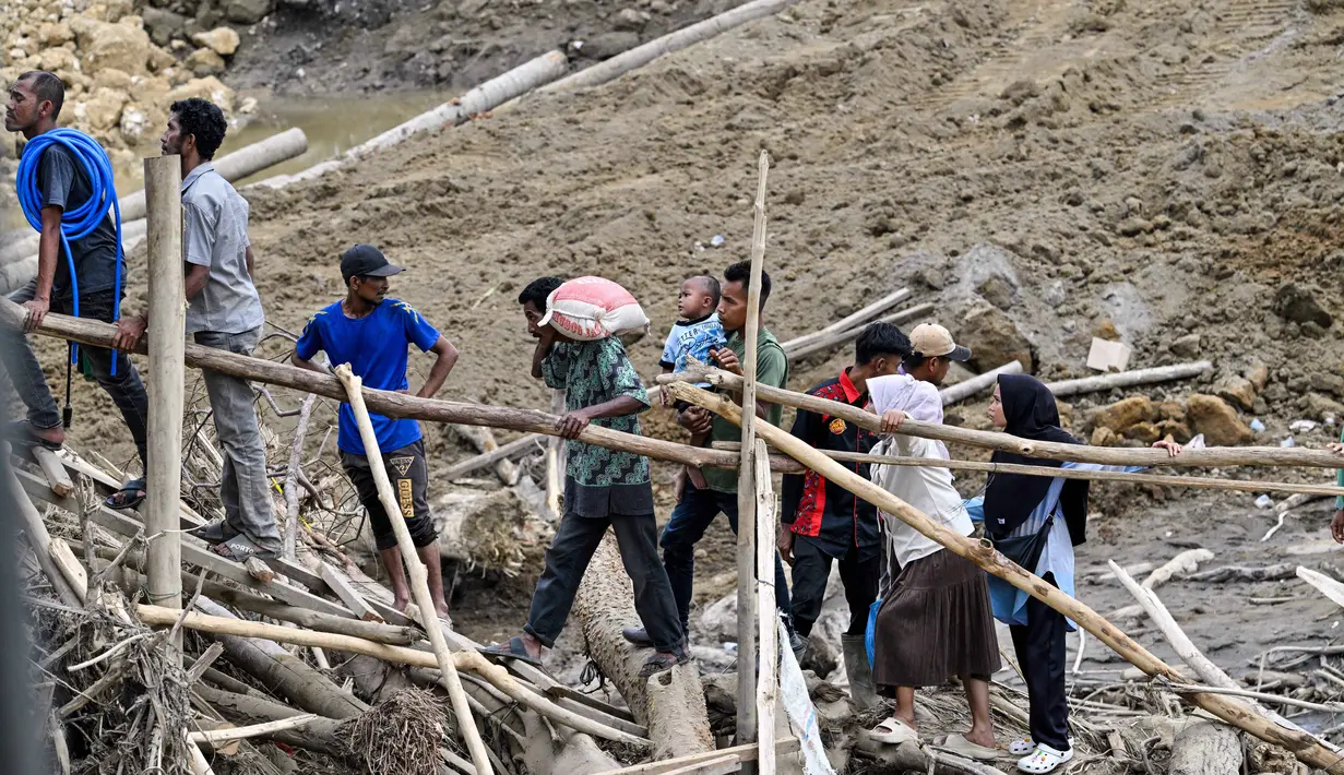 Struktur jembatan baja tersebut ditargetkan menjadi penghubung sementara agar mobilitas masyarakat dan distribusi logistik ke wilayah terdampak dapat kembali berjalan. Tampak dalam foto, warga menyeberangi sungai di jembatan yang baru dibangun yang menghubungkan Aceh dan Provinsi Sumatera Utara setelah hancur akibat banjir bandang di Sungai Peusangan, Distrik Bireuen, Provinsi Aceh, Selasa 9 Desember 2025. (CHAIDEER MAHYUDDIN/AFP)