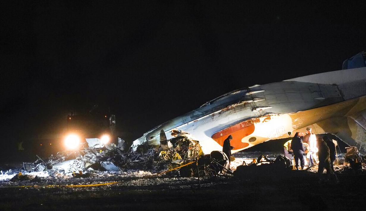 Pekerja darurat bekerja di samping pesawat Antonov An-26 yang jatuh di Bandara Almaty, Kazakhstan, Sabtu (13/3/2021). Antonov An-26 merupakan pesawat transportasi militer buatan Rusia. (AP Photo/Vladimir Tretyakov)