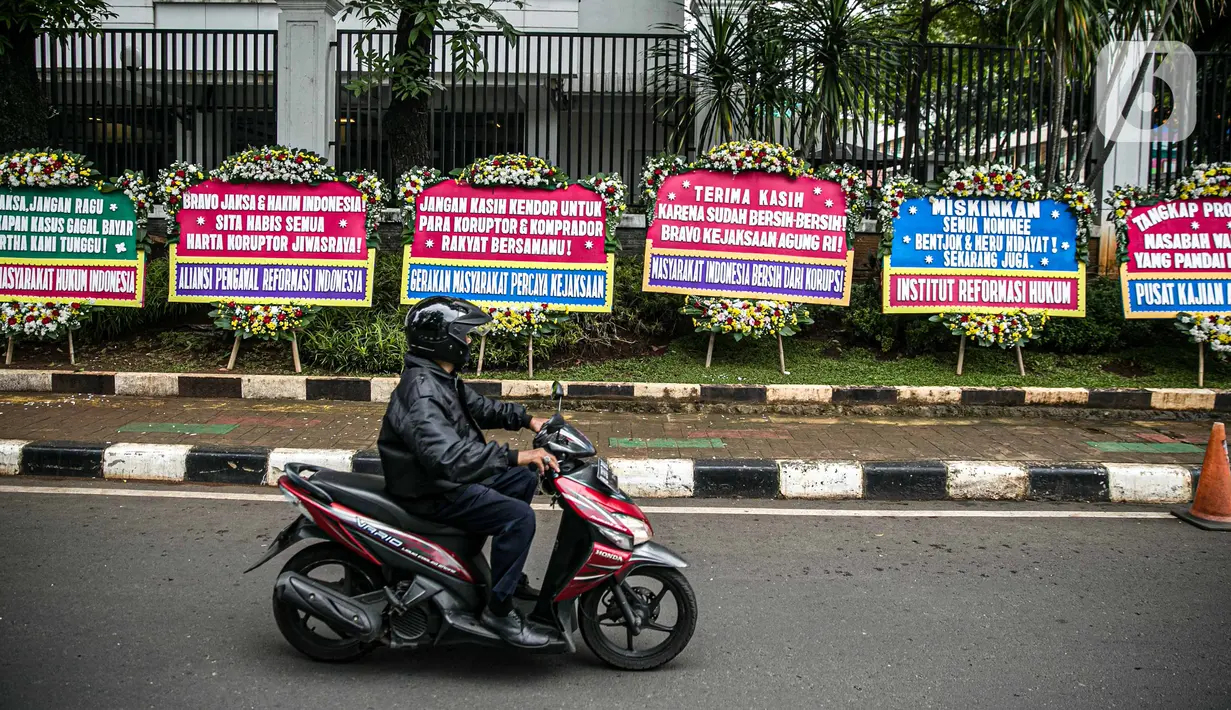 Pengendara melintasi karangan bunga di depan Gedung Kejaksaan Agung RI, Jakarta, Selasa (27/10/2020). Karangan bunga berasal dari korban terdampak kasus asuransi Jiwasraya yang mengharapkan kasus mega skandal itu bisa segera tuntas dan memberikan keadilan bagi mereka. (Liputan6.com/Faizal Fanani)