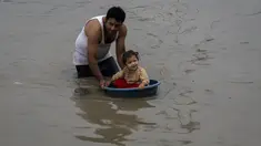 Seorang pria meletakkan anaknya di wadah plastik untuk bermain di air banjir sungai Bagmati setelah hujan deras di Kathmandu, Nepal, Selasa (8/8/2023). (AP Photo/Niranjan Shrestha)