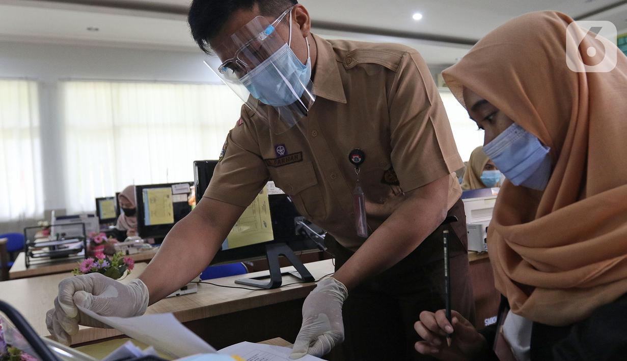 Guru sedang memeriksa tugas murid di SMKN 51, Jakarta, Rabu (7/4/2021). Para murid diwajibakan membawa makanan sendiri  dan mengikuti syarat & panduan sekolah tatap muka seperti membuka pintu dan jendela.(Liputan6.com/Herman Zakharia)