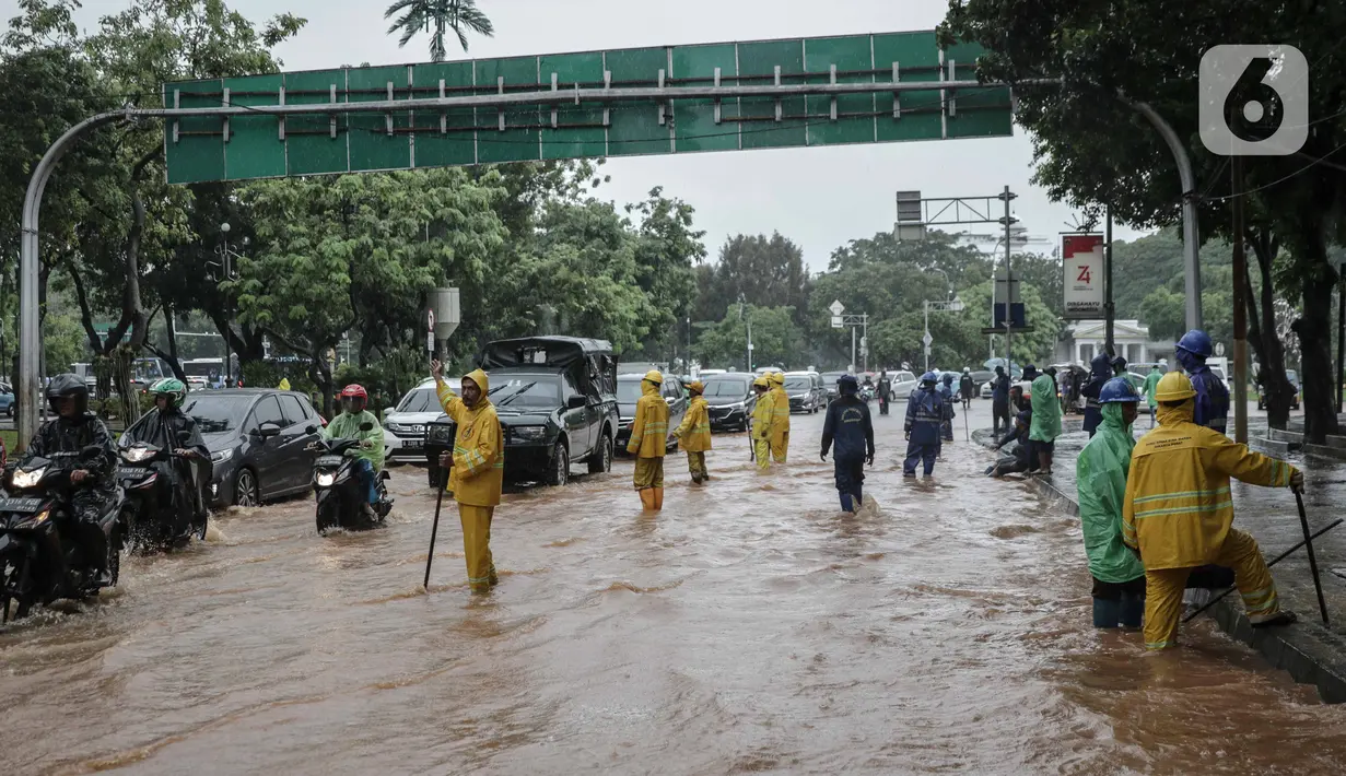 Petugas mengatur lalu lintas saat air menggenangi Jalan Medan Merdeka Barat, Jakarta, Kamis (24/1/2020). Hujan deras yang mengguyur Jakarta sejak pagi tadi mengakibatkan genangan air di Jalan Medan Merdeka Barat. (Liputan6.com/Faizal Fanani)