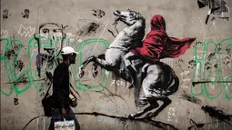 Seorang pria berjalan melewati mural yang diduga karya seniman sekaligus aktivis Banksy di Paris, Prancis, Minggu (24/6). Banksy menyoroti kebijakan pemerintah yang menomorduakan pencari suaka di Eropa. (PHILIPPE LOPEZ/AFP)