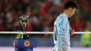Penyerang Argentina, Lionel Messi tertunduk di samping trofi usai negaranya dikalahkan Chili di final Copa America 2015 di Stadion Nasional, Chili, (4/7/2015). Chili menang lewat adu penalti atas Argentina dengan skor 4-1. (REUTERS/Ivan Alvarado)