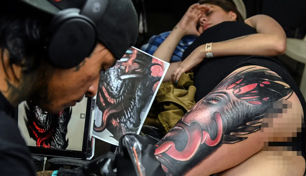 Seorang wanita terbaring saat membuat tato dikakinya selama Expotattoo Colombia 2019 di Medellin, departemen Antioquia (2/6/2019). Para penggila tato antusias untuk mentato tubuhnya di festival tato terbesar di negara tersebut. (AFP Photo/Joaquim Sarmiento)