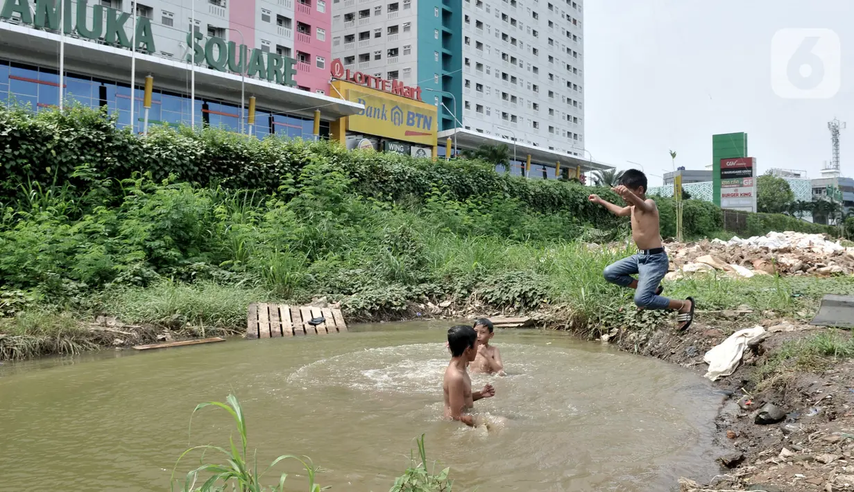 Anak-anak berenang di kubangan air di depan Apartemen Green Pramuka, Jakarta, Rabu (5/2/2020). Keterbatasan ekonomi dan minimnya lahan bermain membuat sekelompok anak sekolah dasar ini memilih berenang di kubangan meskipun mereka tahu air kotor dapat menimbulkan penyakit. (merdeka.com/Iqbal Nugroho)