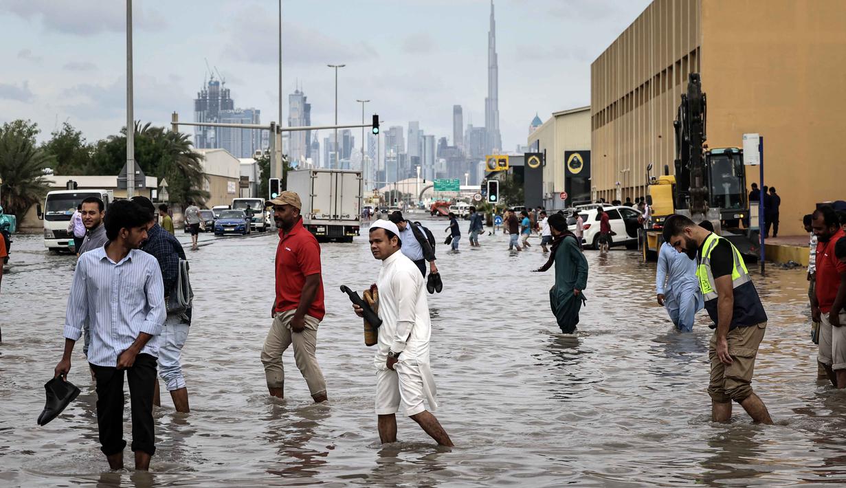 Orang-orang menerobos genangan air banjir setelah hujan lebat di Dubai, Uni Emirat Arab (UEA) pada Jumat 19 Desember 2025. Hujan lebat yang terjadi pada Jumat 19 Desember 2025 berimbas pada genangan banjir di sejumlah ruas jalan di Dubai, Uni Emirat Arab (UEA). (FADEL SENNA/AFP)