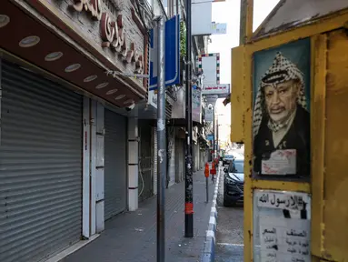 Potret mendiang pemimpin Palestina Yasser Arafat dipajang di samping toko-toko yang tutup selama pemogokan umum di kota Tepi Barat, Ramallah, pada 11 Desember 2023. (Jaafar ASHTIYEH/AFP)